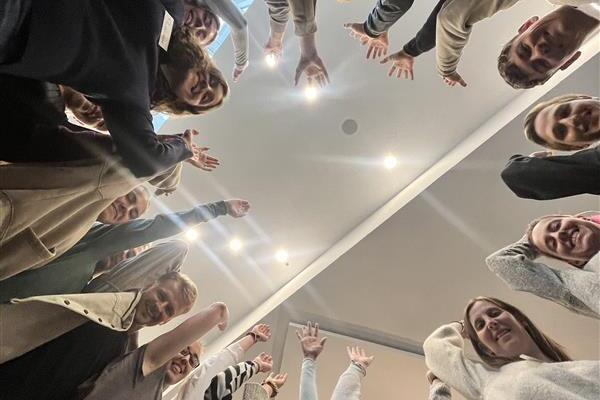 Gruppe von Menschen aus der Froschperspektive, die freudig die Arme nach oben strecken, unter einer Deckenlampe.