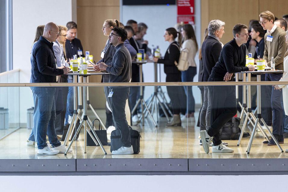 Netzwerkveranstaltung mit mehreren Personen an Stehtischen, im Hintergrund Gespräche und erfrischende Getränke.