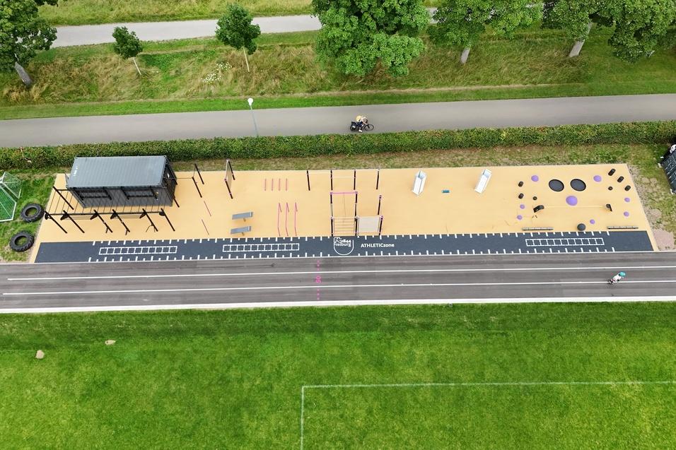 Luftaufnahme eines modernen Outdoor-Fitnessbereichs mit Geräten und Trainingsstationen auf einem Sandboden.