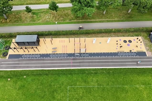 Luftaufnahme eines modernen Outdoor-Fitnessbereichs mit Ger&auml;ten und Trainingsstationen auf einem Sandboden.