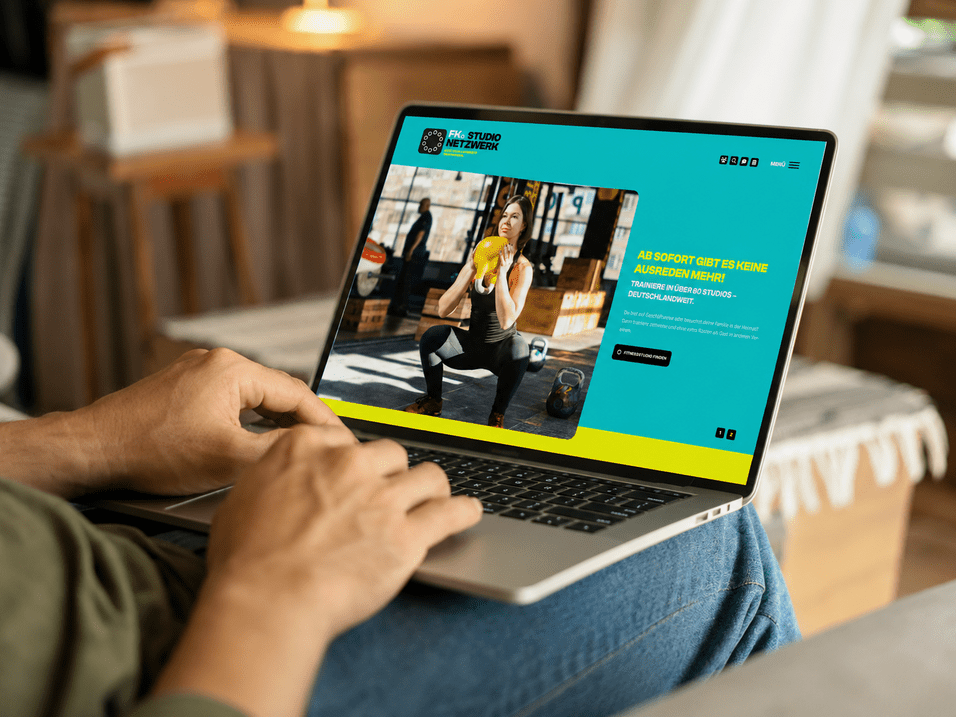 Person betrachtet eine Webseite mit Fitnessangeboten auf einem Laptop in einem gemütlichen Raum.