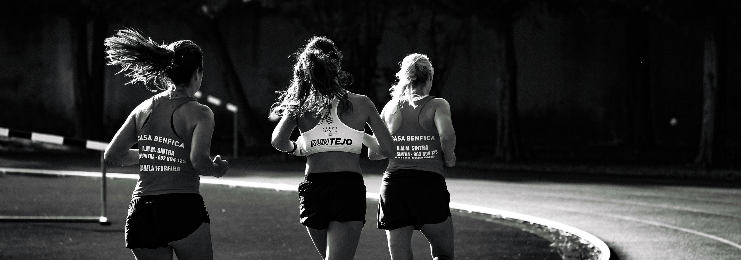 Drei Frauen in Sportkleidung joggen auf einer kurvenreichen Laufbahn in Schwarz-Wei&szlig;.